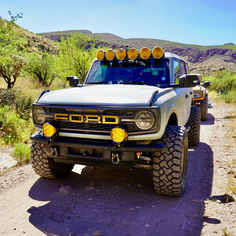 A gray Ford Bronco equipped with two Suparee Helm 7 inch amber LED pods mounted on the front bumper driving on a desert trail.