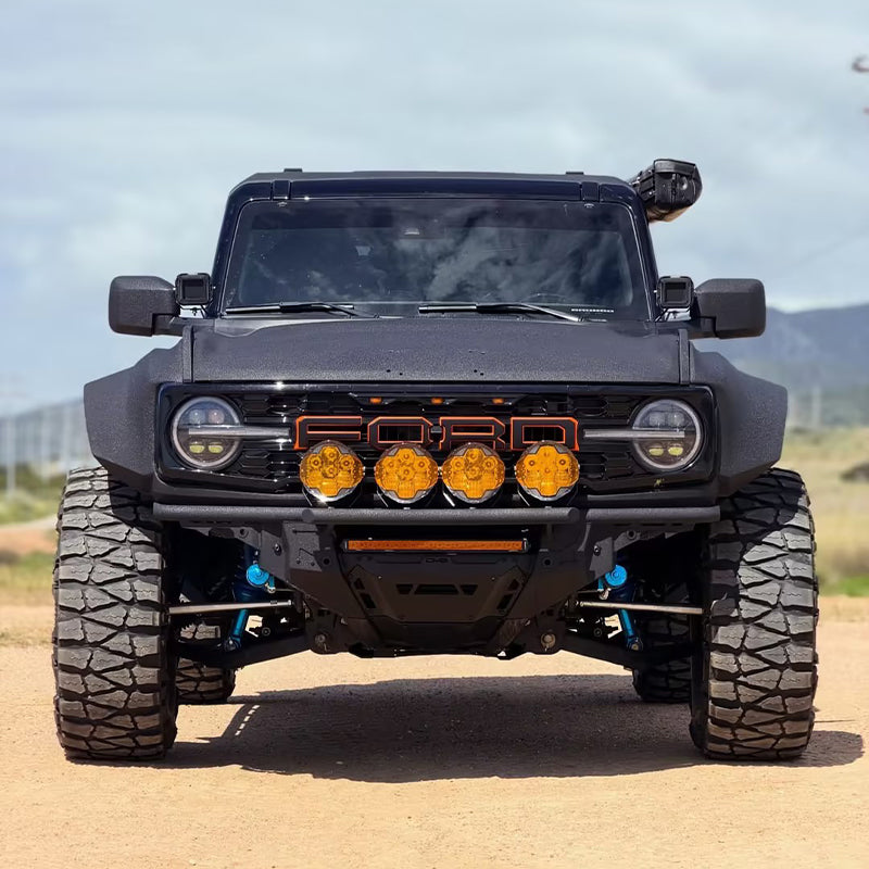 Four Suparee Helm 7 series round amber LED driving lights installed on the front bumper grille guard of a matte black Ford Bronco.