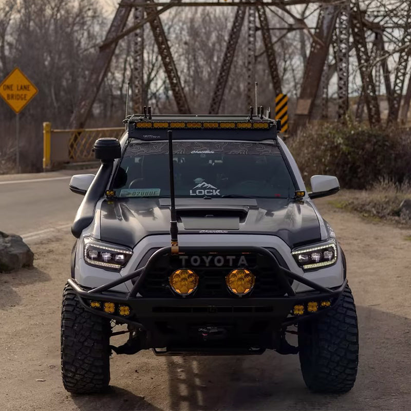 Suparee Helm 7 high-power amber LED pods fitted on the front bull bar of a modified white Toyota Tacoma near a bridge.